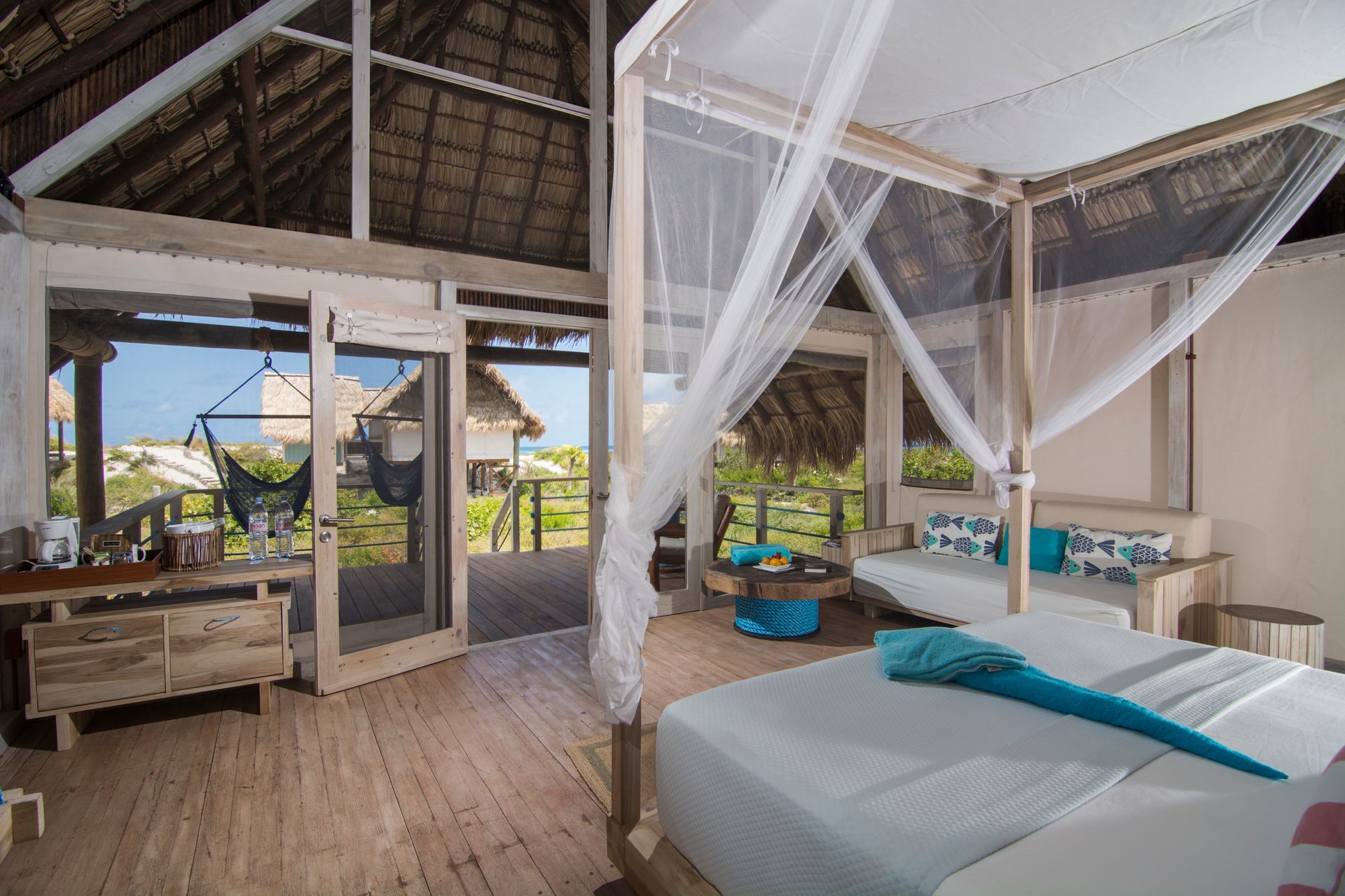Bedroom with four-poster bed, gauzy canopy, and open doors to a deck overlooking a tropical view.