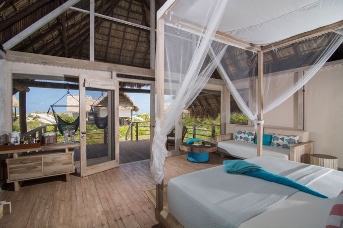 Bedroom with four-poster bed, gauzy canopy, and open doors to a deck overlooking a tropical view.