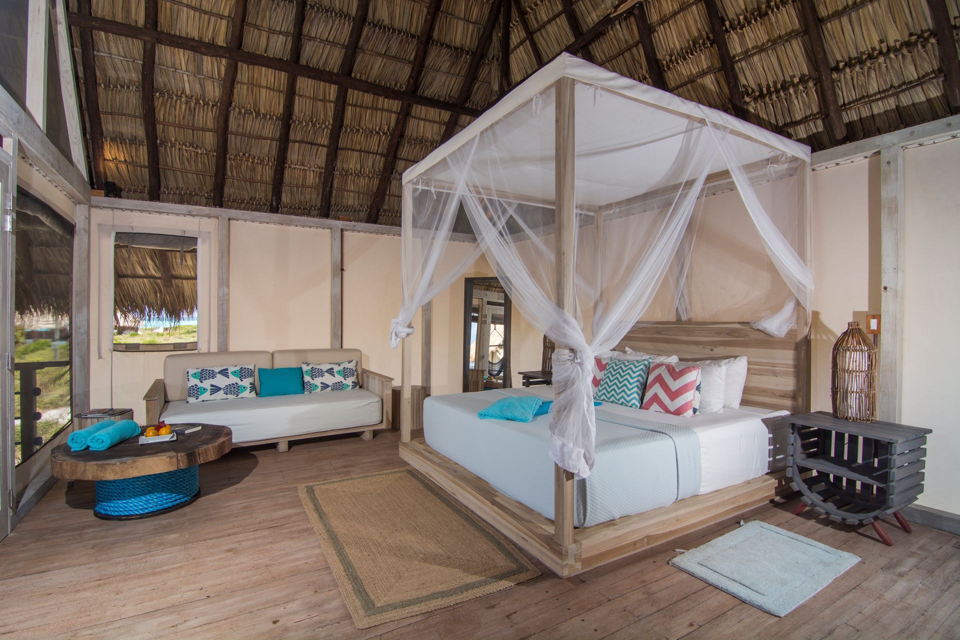 Bedroom with canopy bed, sofa, and thatched roof. Wooden floors and neutral tones.