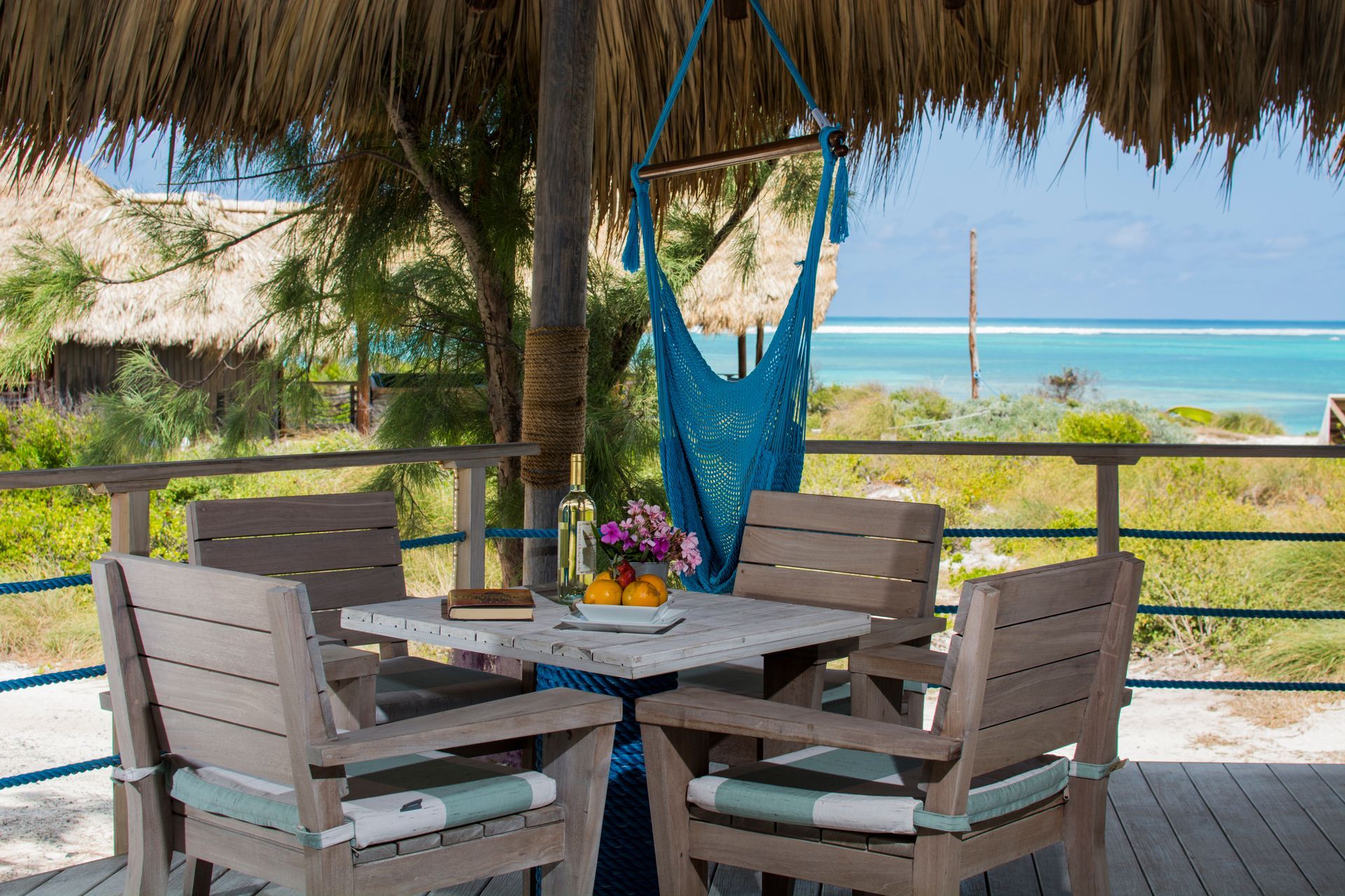 Patio table and chairs under a thatched roof, overlooking the turquoise ocean.