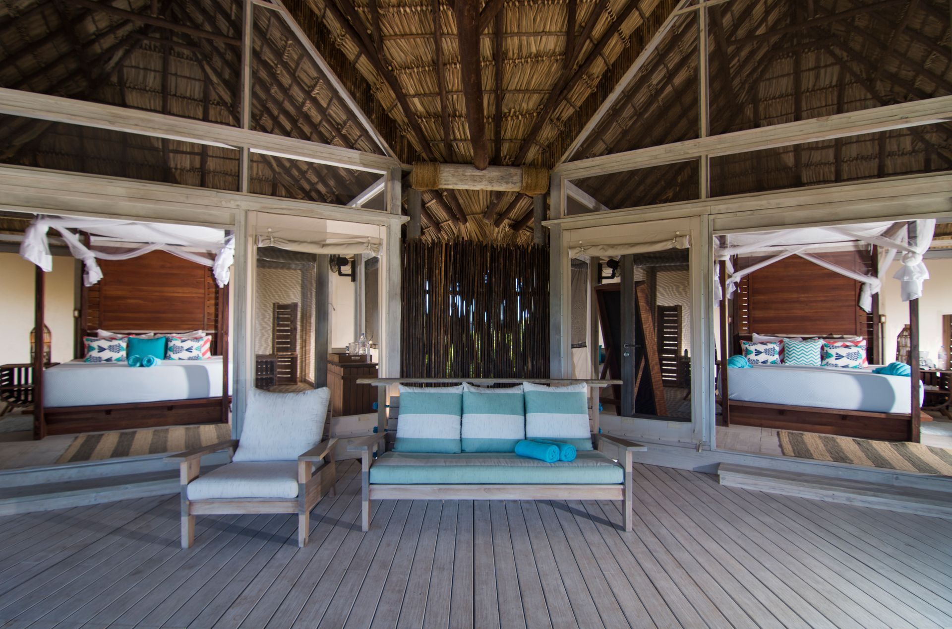 Open-air luxury bedroom with two beds, a sofa, and thatched roof, with ocean views.