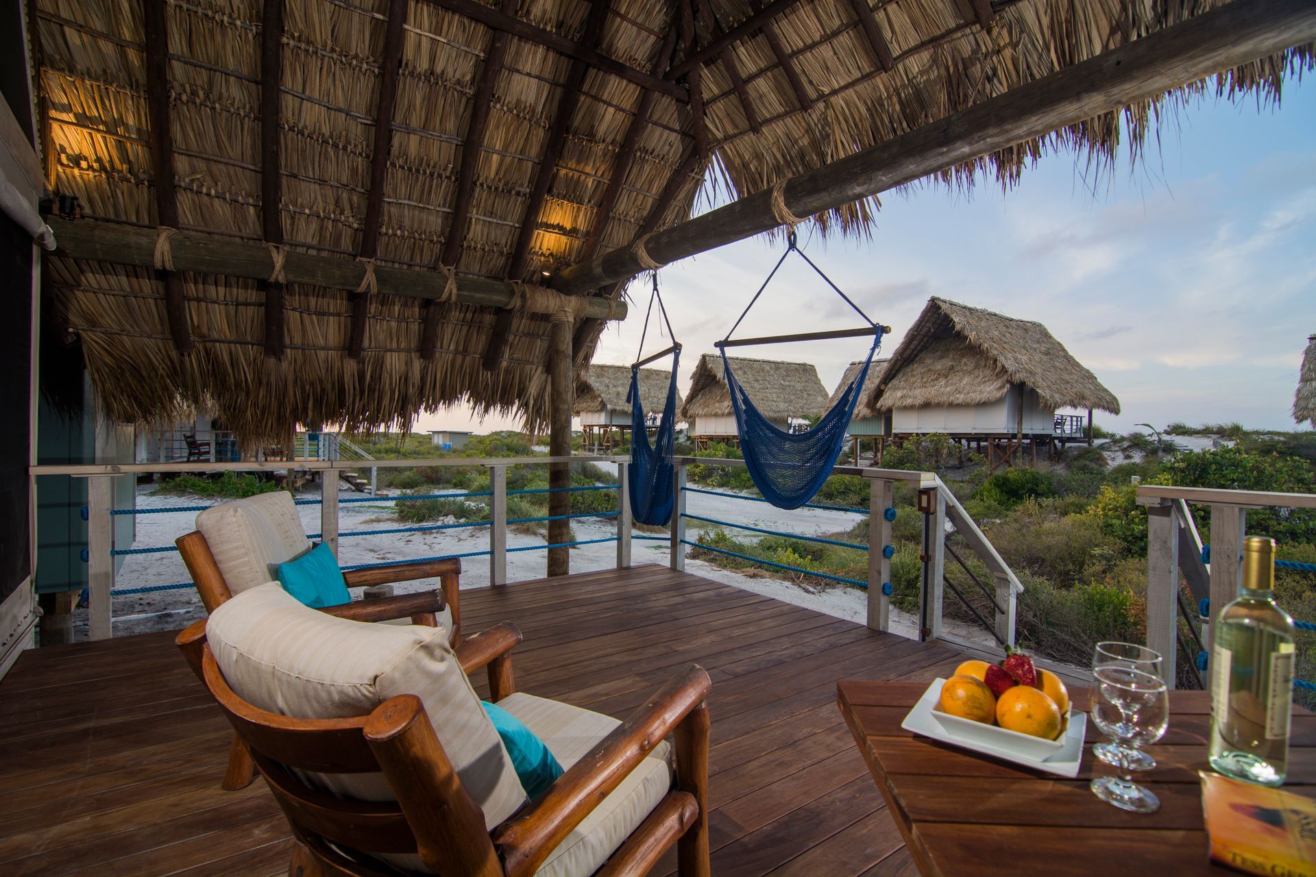 Porch with wooden chairs, hammock, table with fruit, and ocean view.