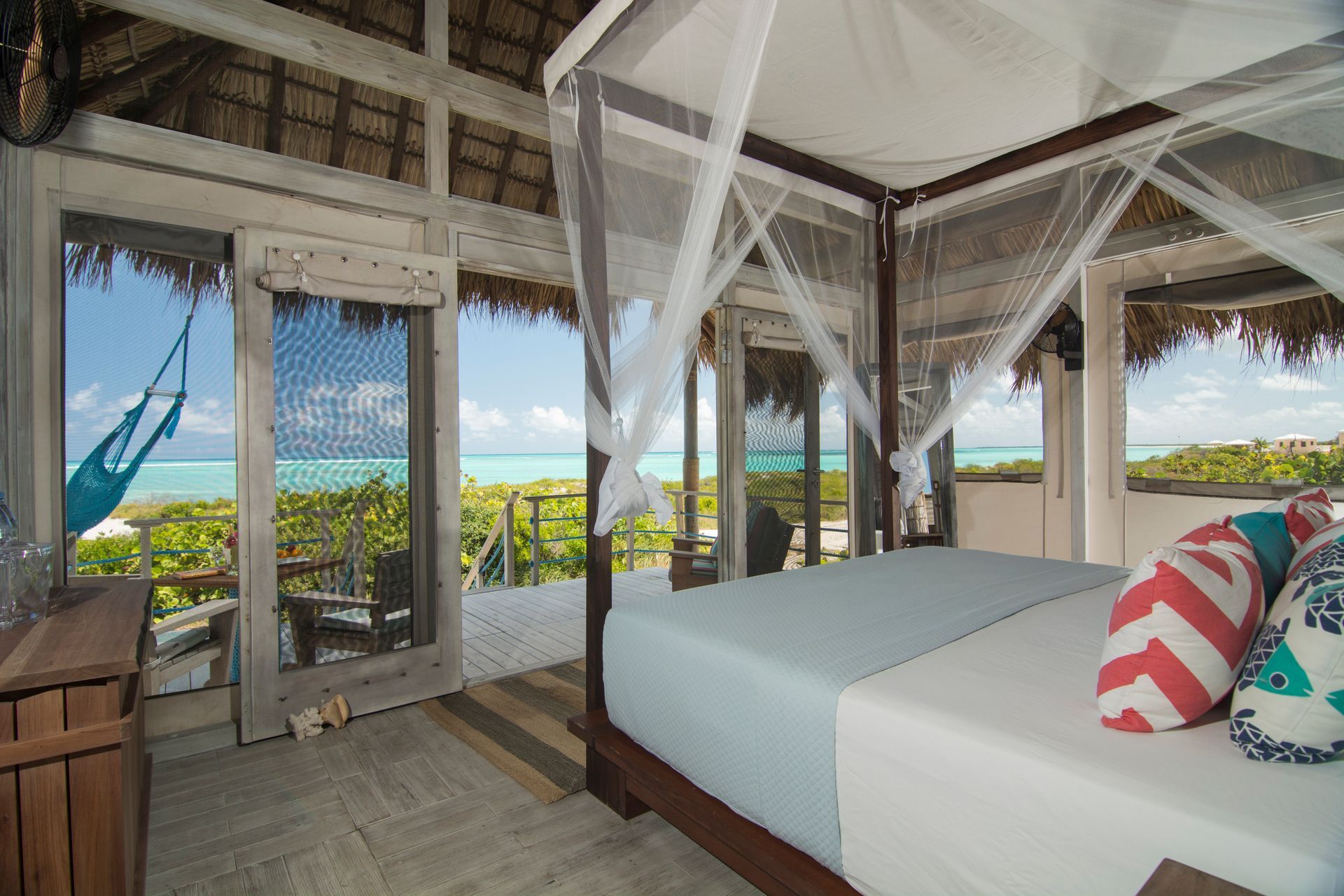 Bedroom with canopy bed, open doors overlooking a beach and turquoise water.
