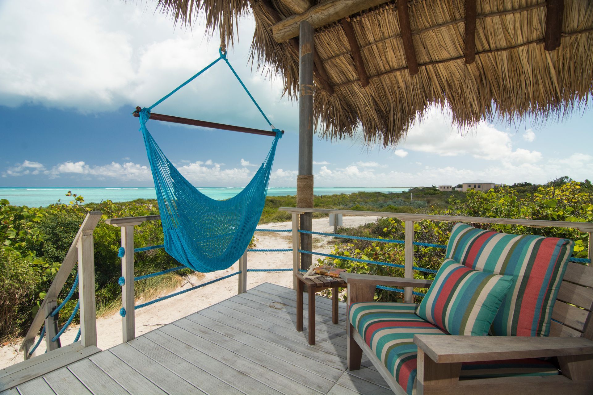 Tropical porch with hammock and chair overlooking turquoise ocean.