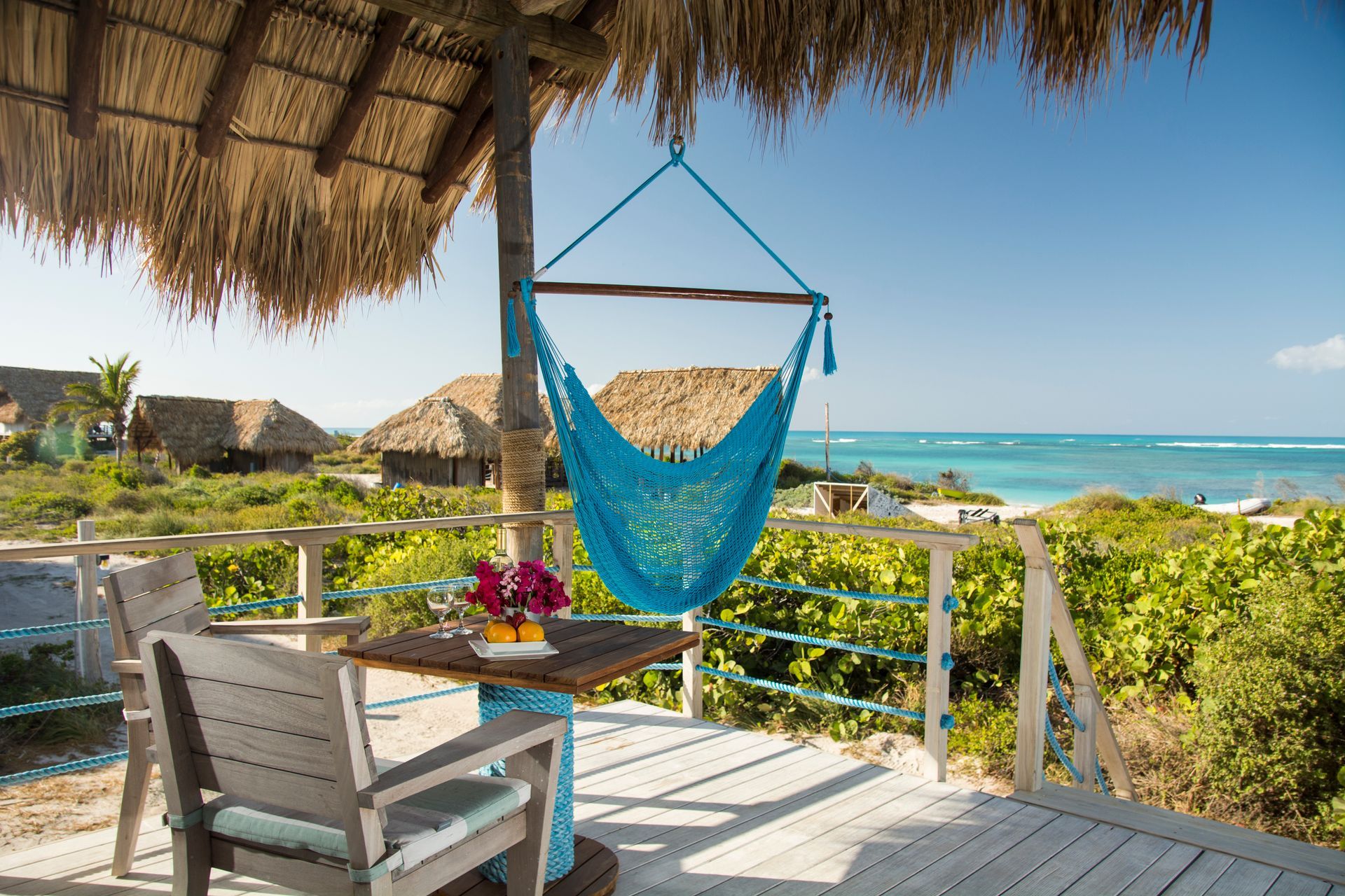 A porch with a hammock and small table, overlooking the ocean. Tropical scene with blue and brown tones.