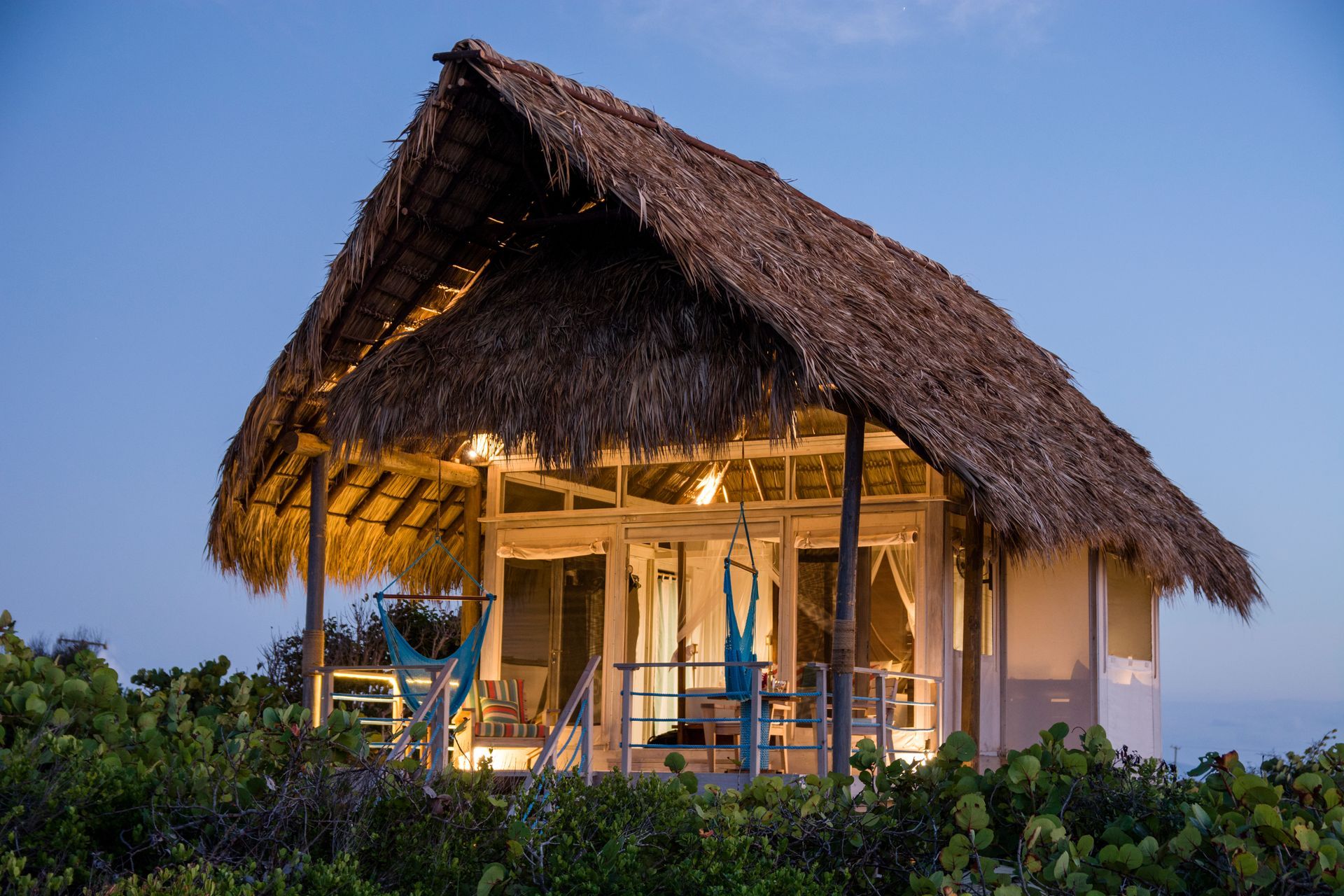 Tropical hut with thatched roof lit at dusk.