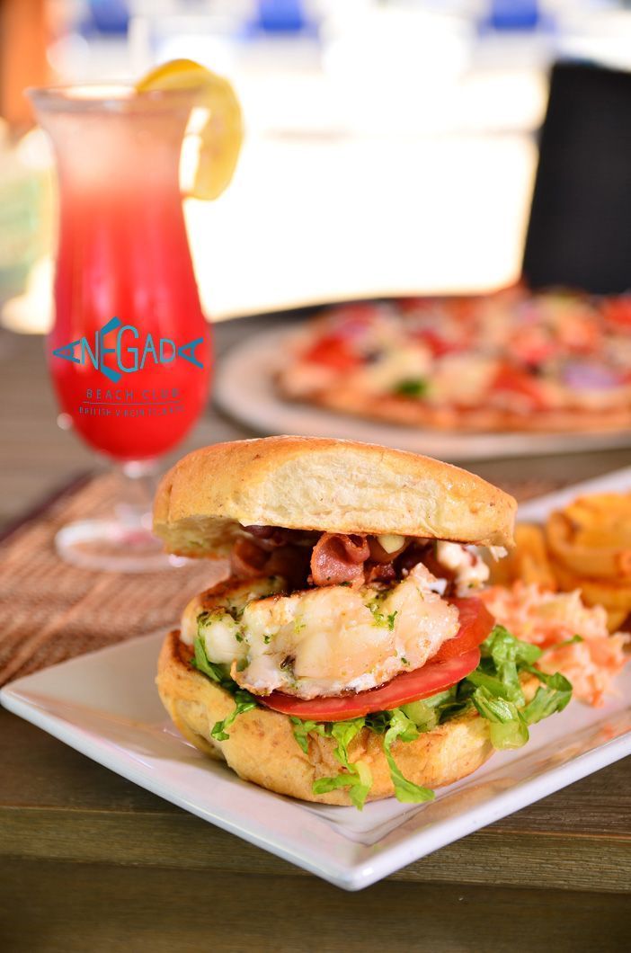 Burger with toppings, a red drink, and pizza on a table at a restaurant.