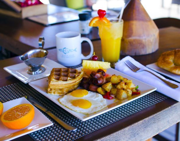 Breakfast plate with waffles, eggs, potatoes, fruit, and orange juice on a table.