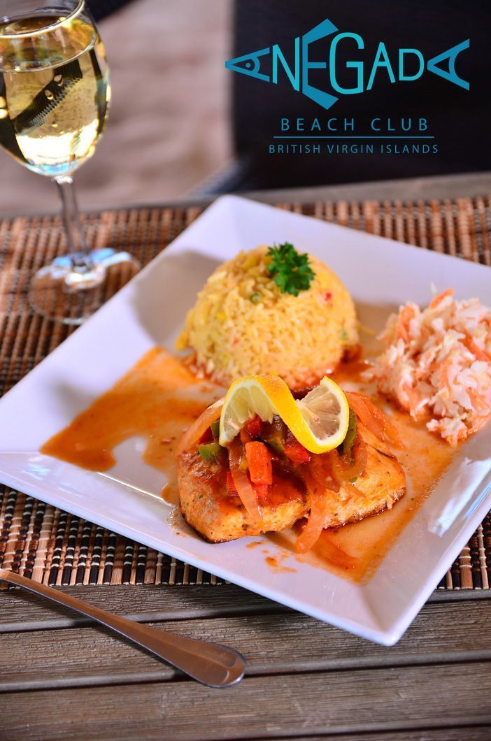 A plate of breaded fish with sauce, rice, and slaw, served with a glass of wine at a beach club.