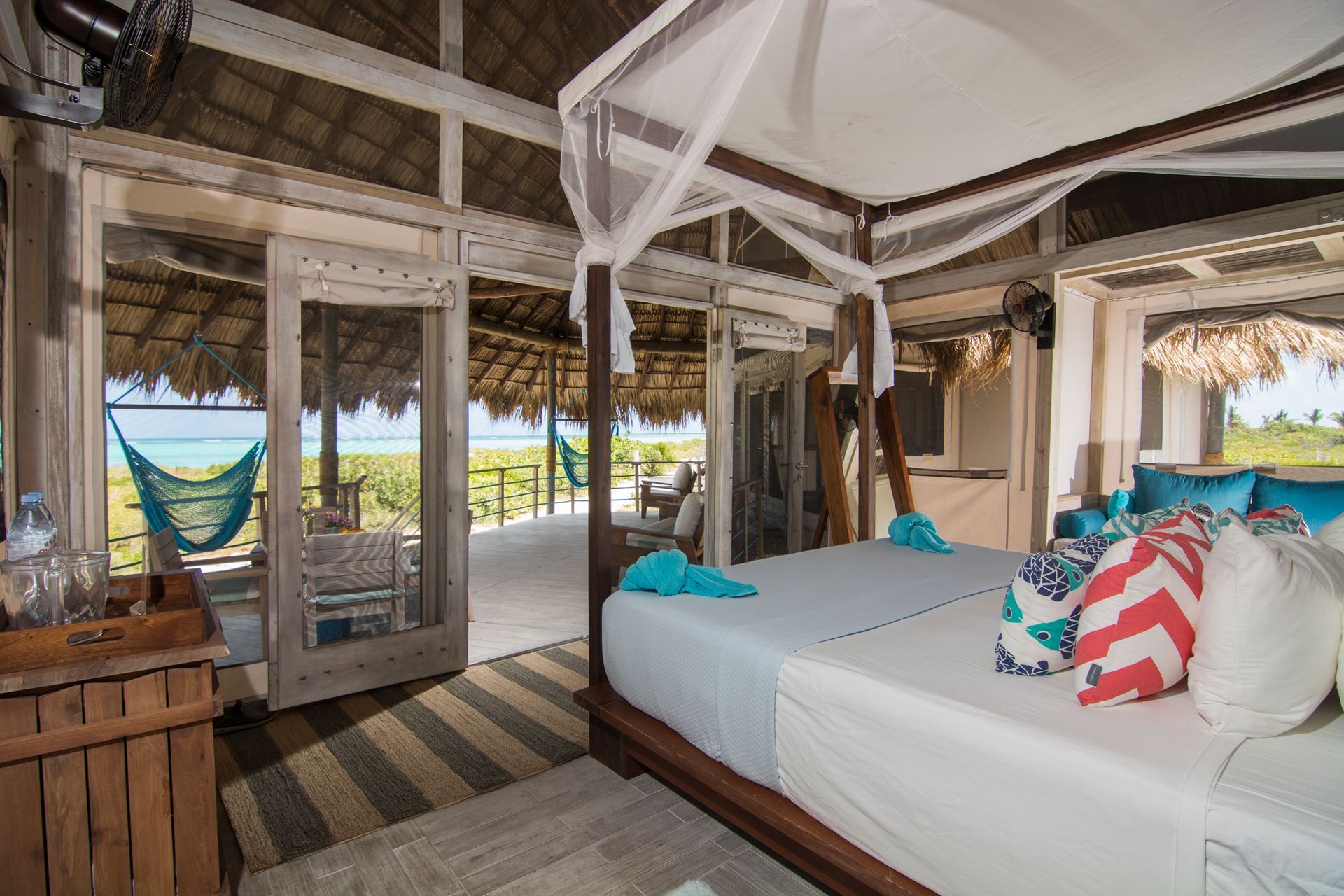 Bedroom with large bed, open doors to deck with hammock overlooking the ocean.