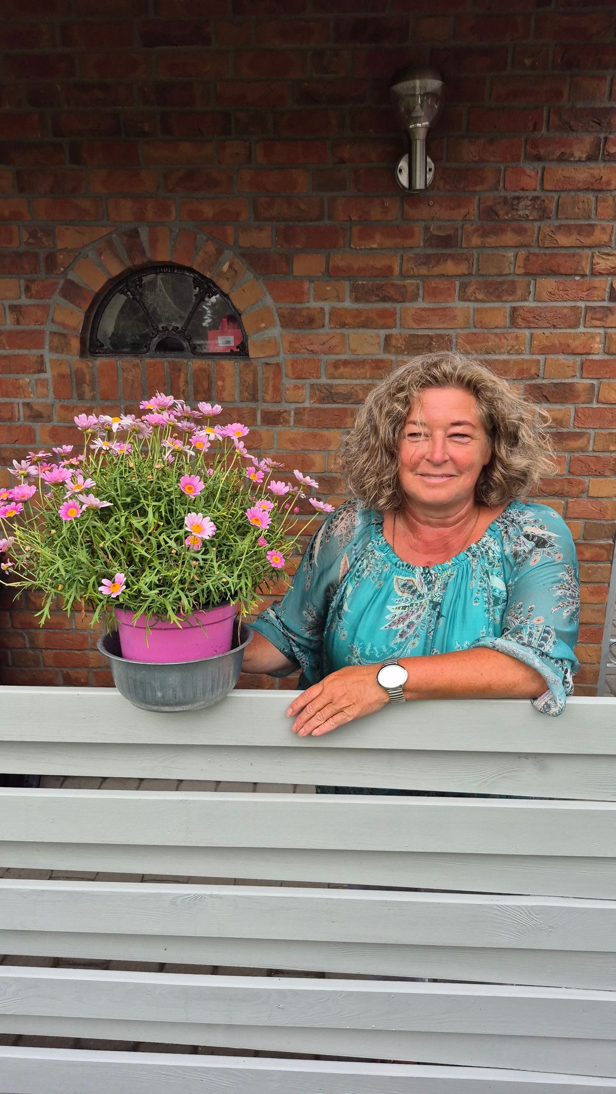Eine Frau lehnt mit Blumen in einem Topf an einem Zaun.