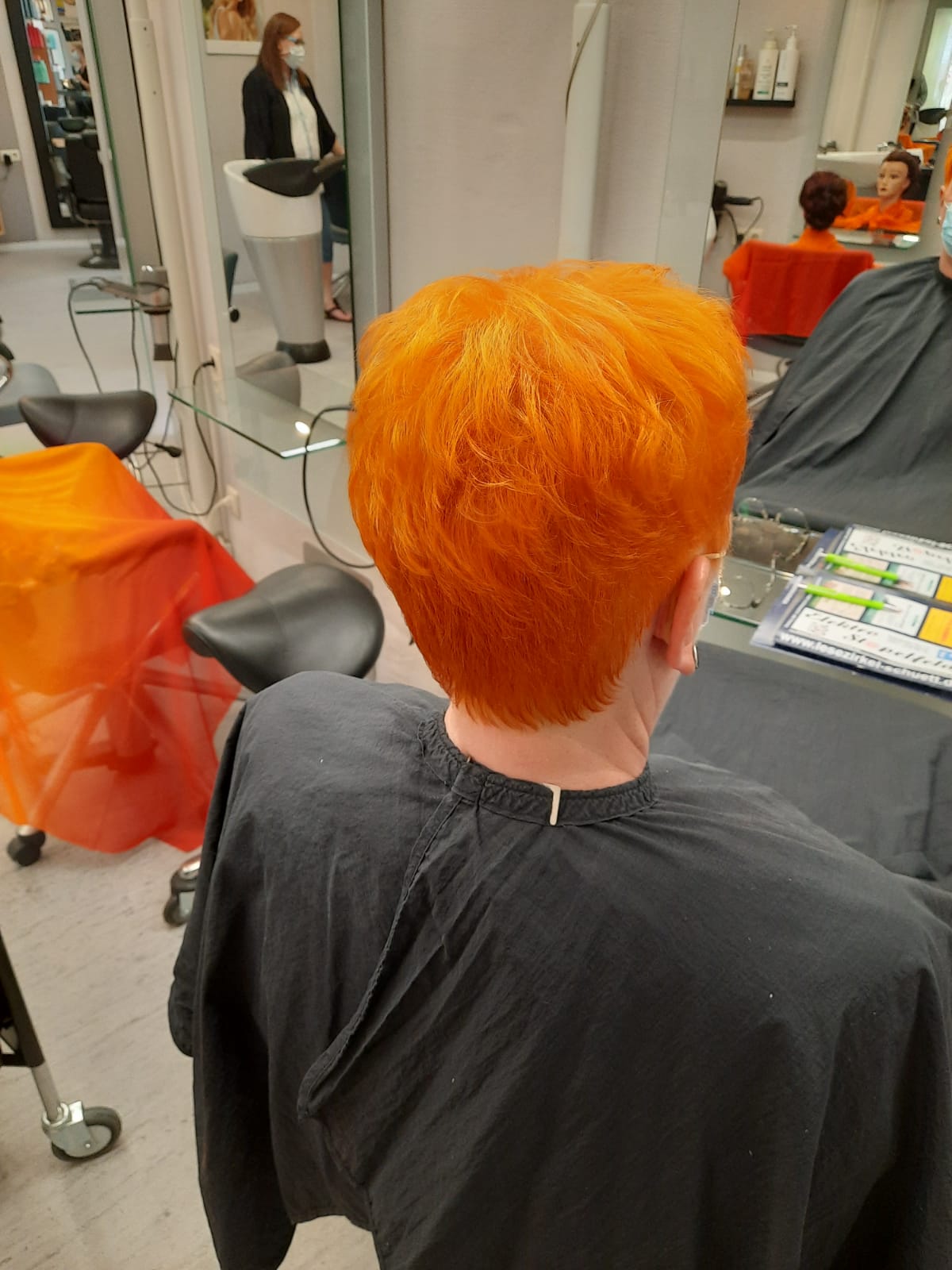 Eine Frau mit leuchtend orangefarbenem Haar lässt sich in einem Salon die Haare schneiden.