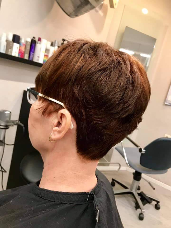 Eine Frau mit kurzen Haaren und Brille sitzt in einem Salon.