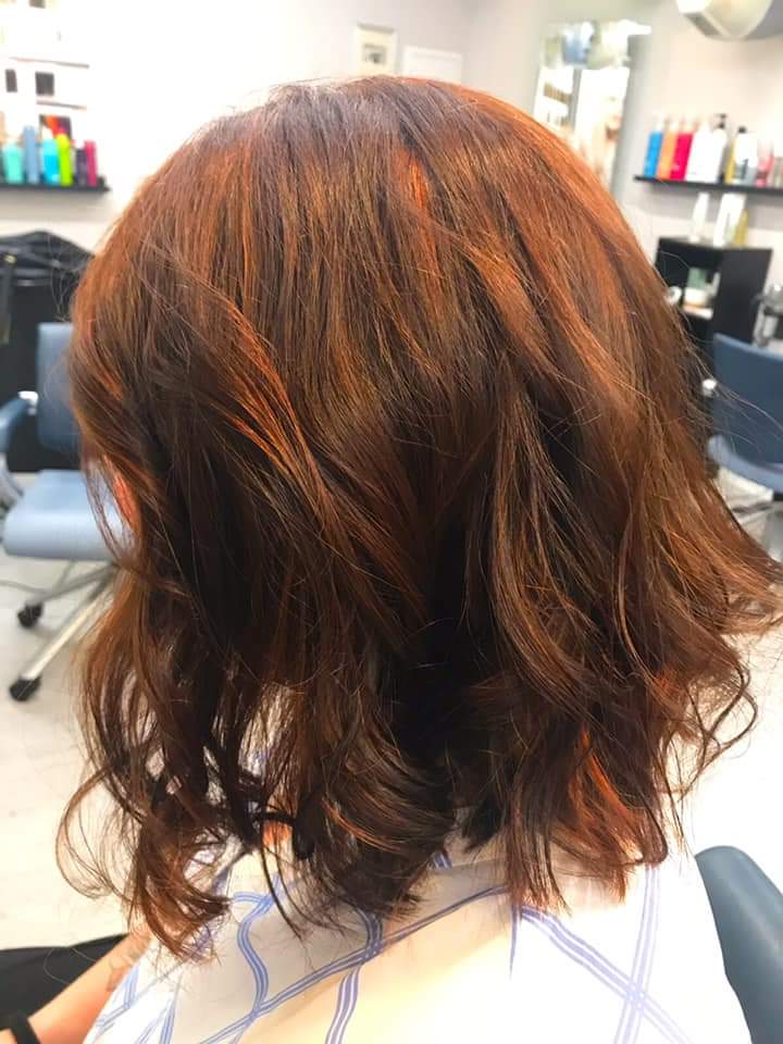 Eine Frau mit langen braunen Haaren sitzt auf einem Stuhl in einem Salon.