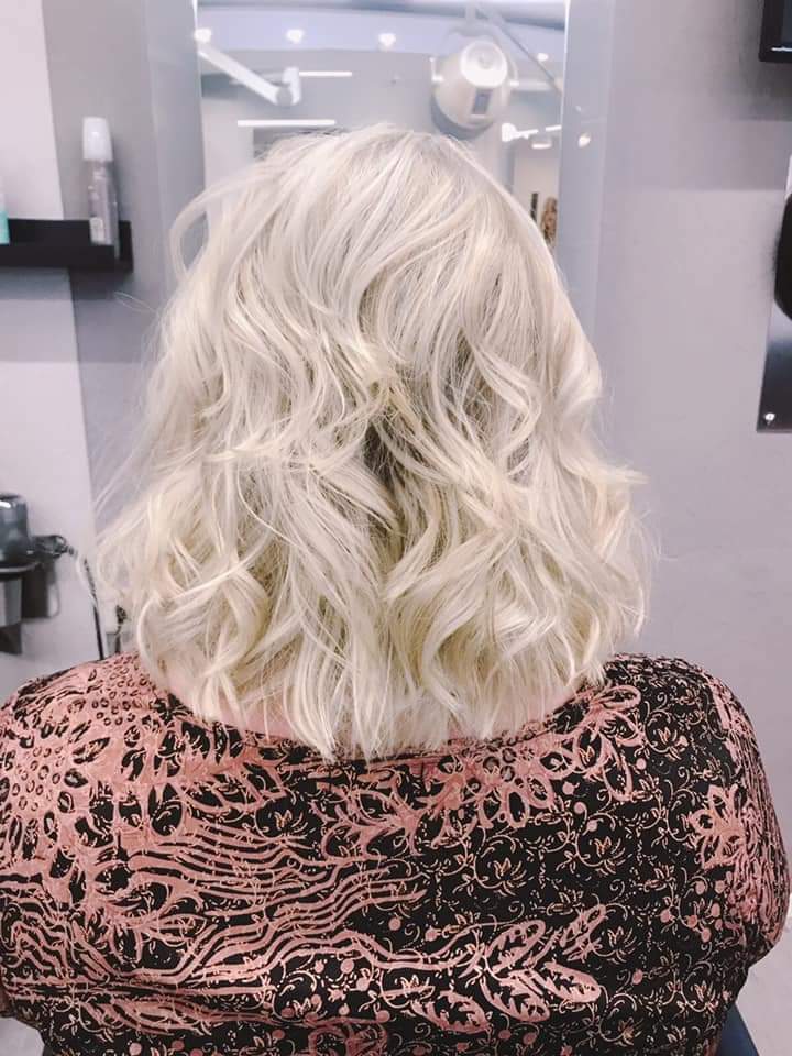 Eine Frau mit blonden Haaren sitzt auf einem Stuhl vor einem Spiegel.