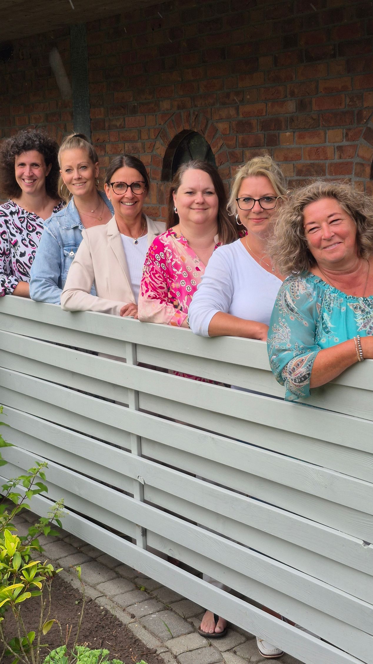 Eine Gruppe von Frauen lehnt an einem weißen Holzzaun.