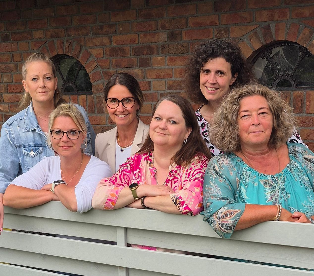 Eine Gruppe von Frauen posiert für ein Foto und lehnt dabei an einem Zaun.