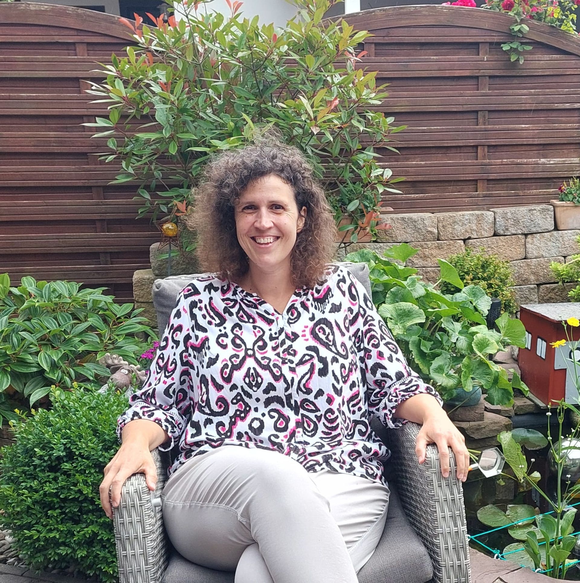 Eine Frau sitzt auf einem Stuhl vor einem Holzzaun.