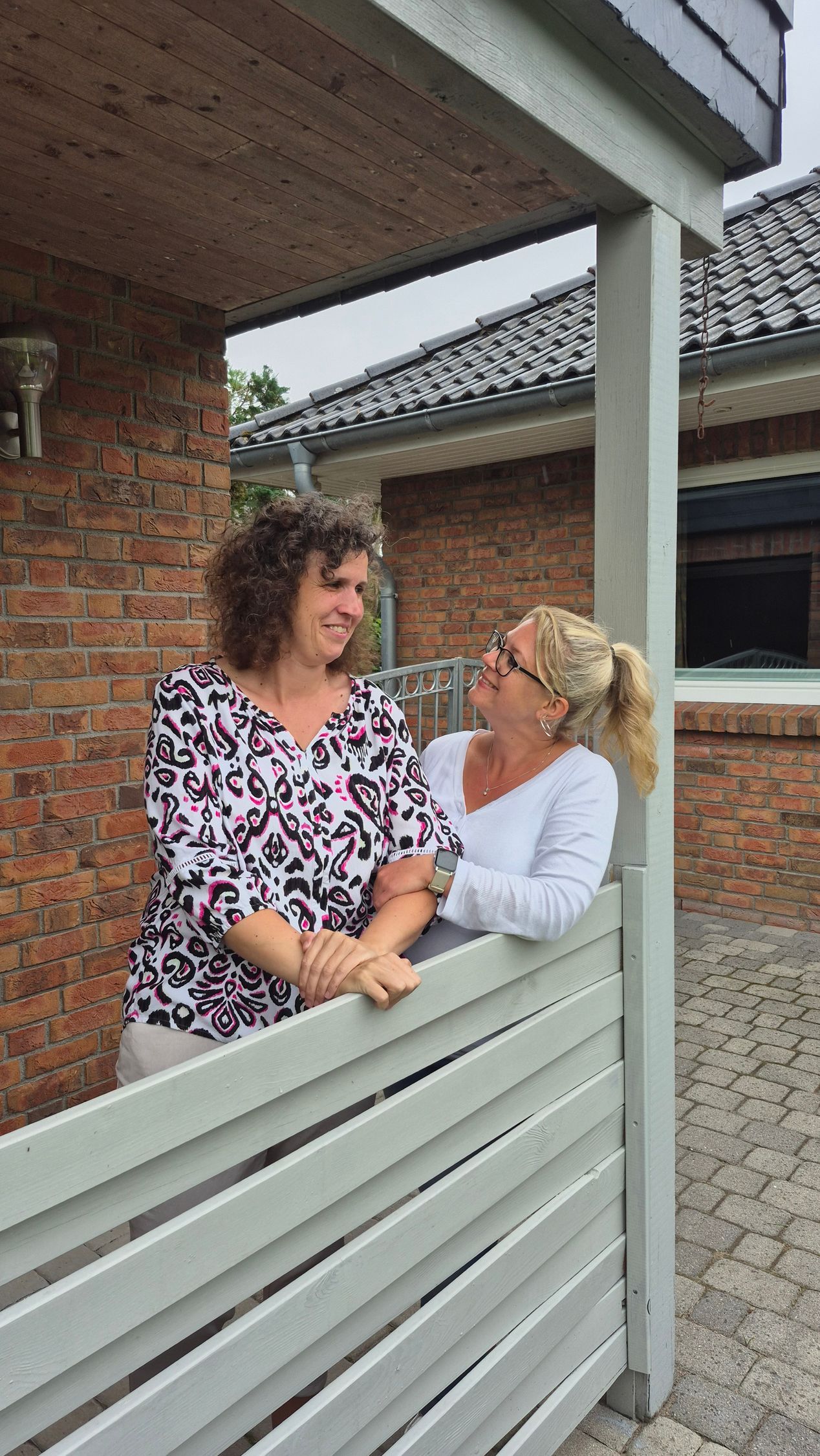 Zwei Frauen stehen nebeneinander auf einer Veranda.