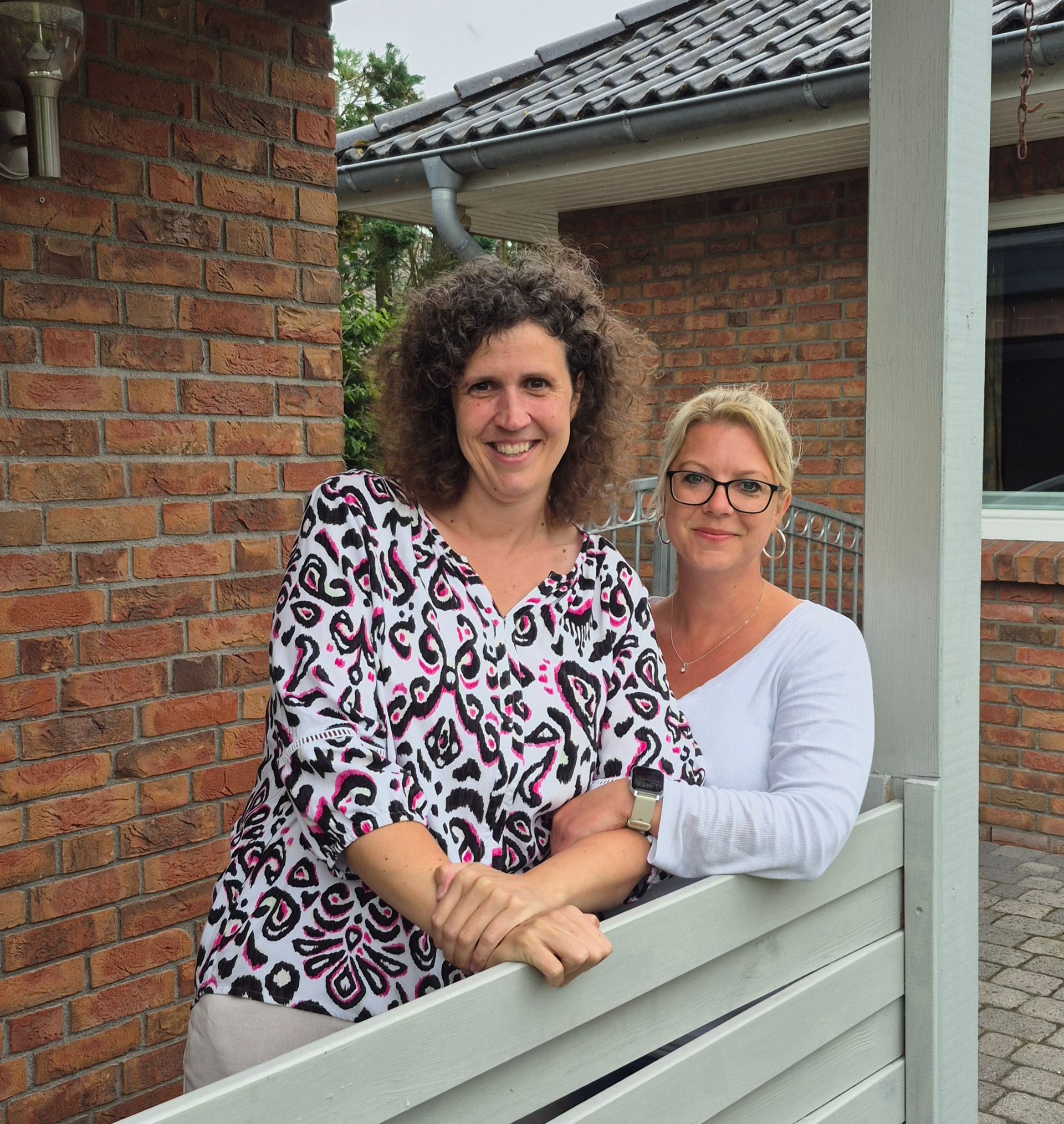 Zwei Frauen posieren für ein Foto vor einem Backsteingebäude