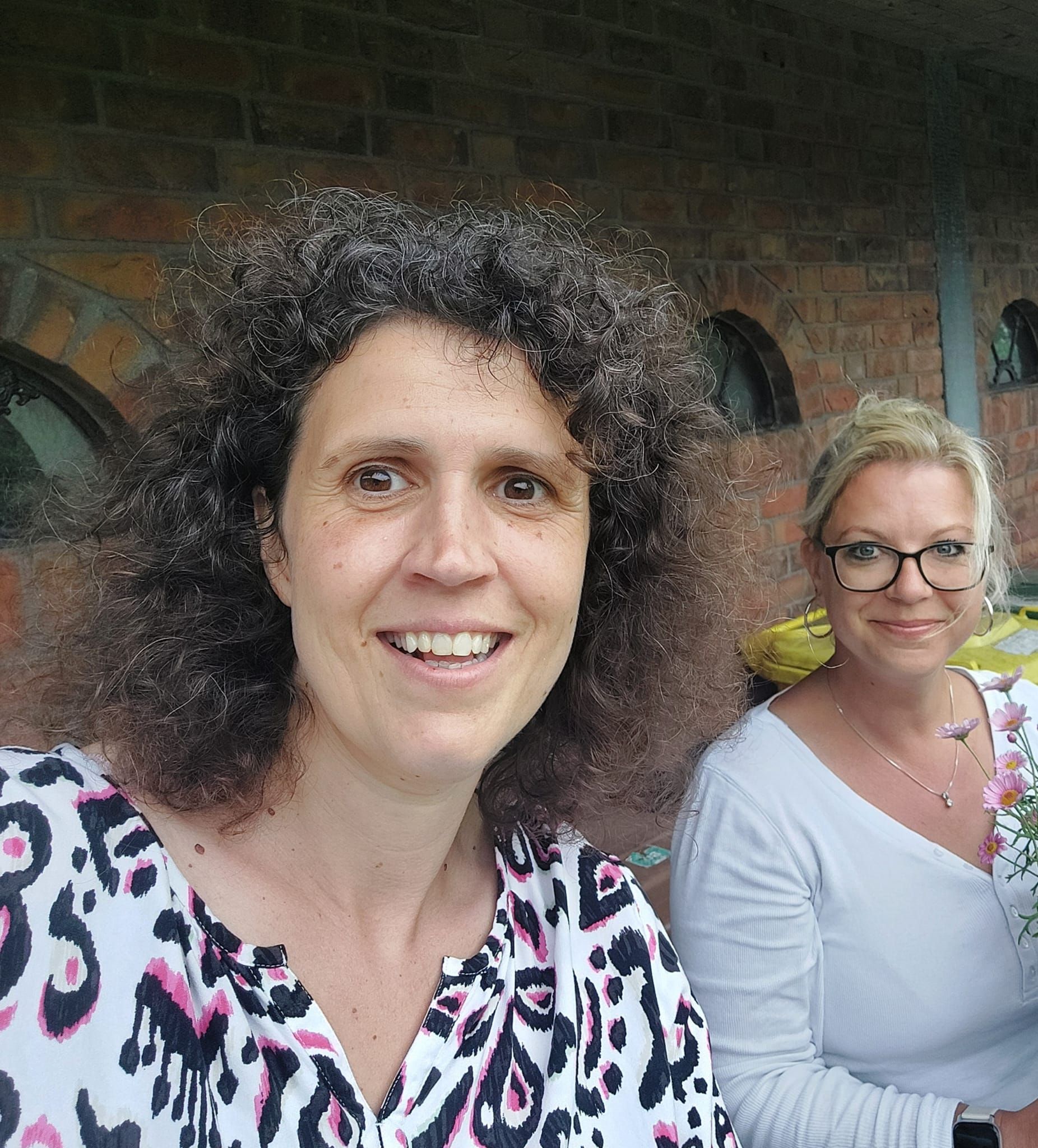 Zwei Frauen posieren vor einer Backsteinmauer für ein Foto.
