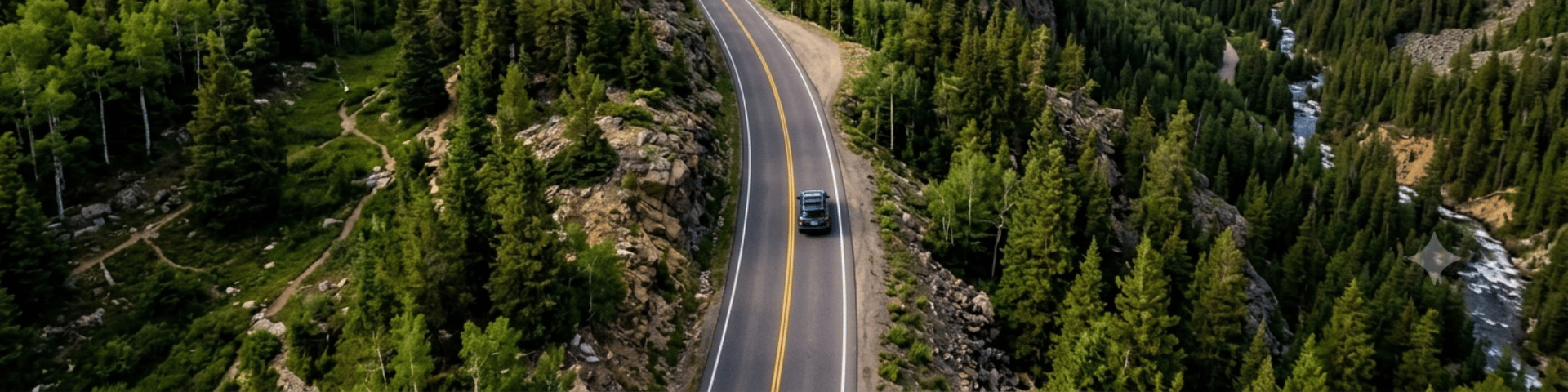 Aerial view of a vehicle driving on a winding mountain road surrounded by dense forest