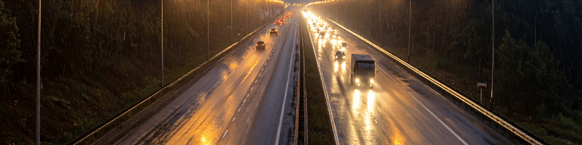 Traffic moving on a wet highway at night with headlights reflecting on the road and rain falling.