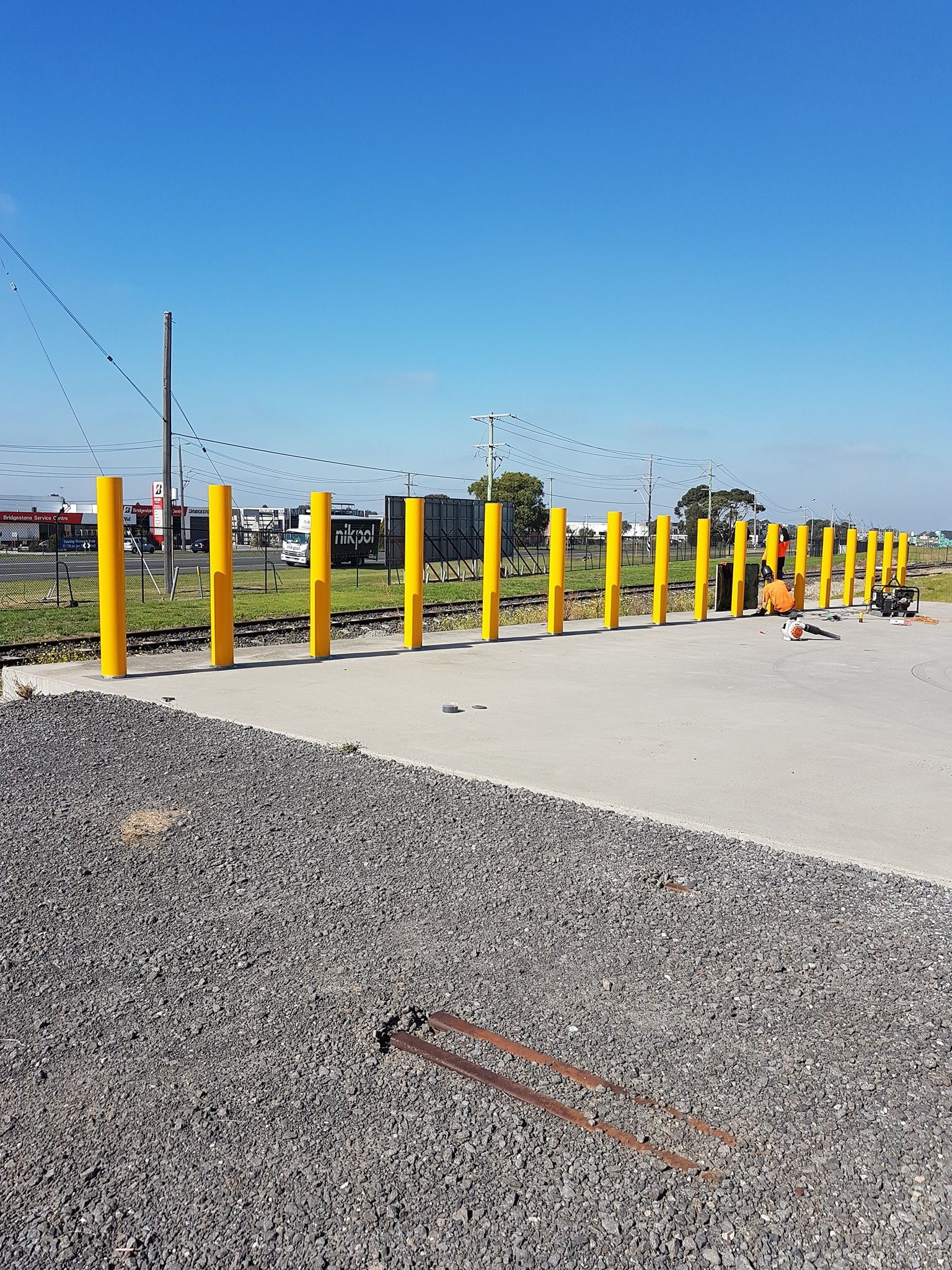 A row of yellow poles are lined up on a gravel road.