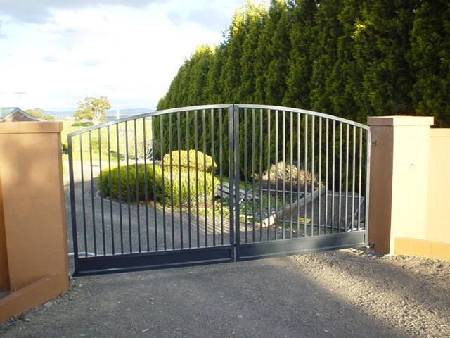 A metal gate is open to a driveway with trees in the background