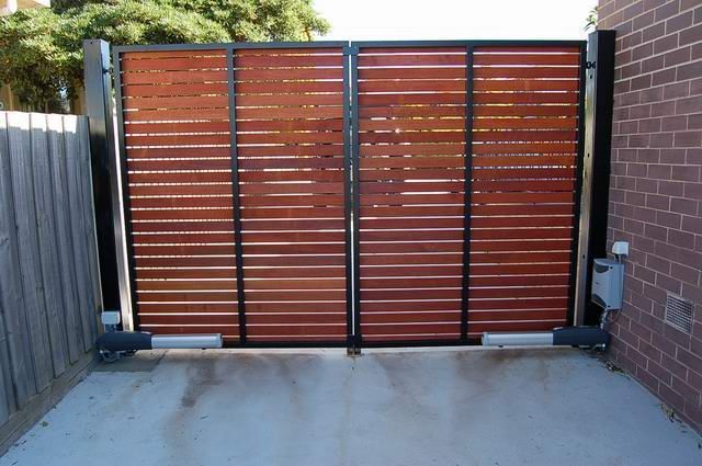 A wooden gate is open in a driveway next to a brick building