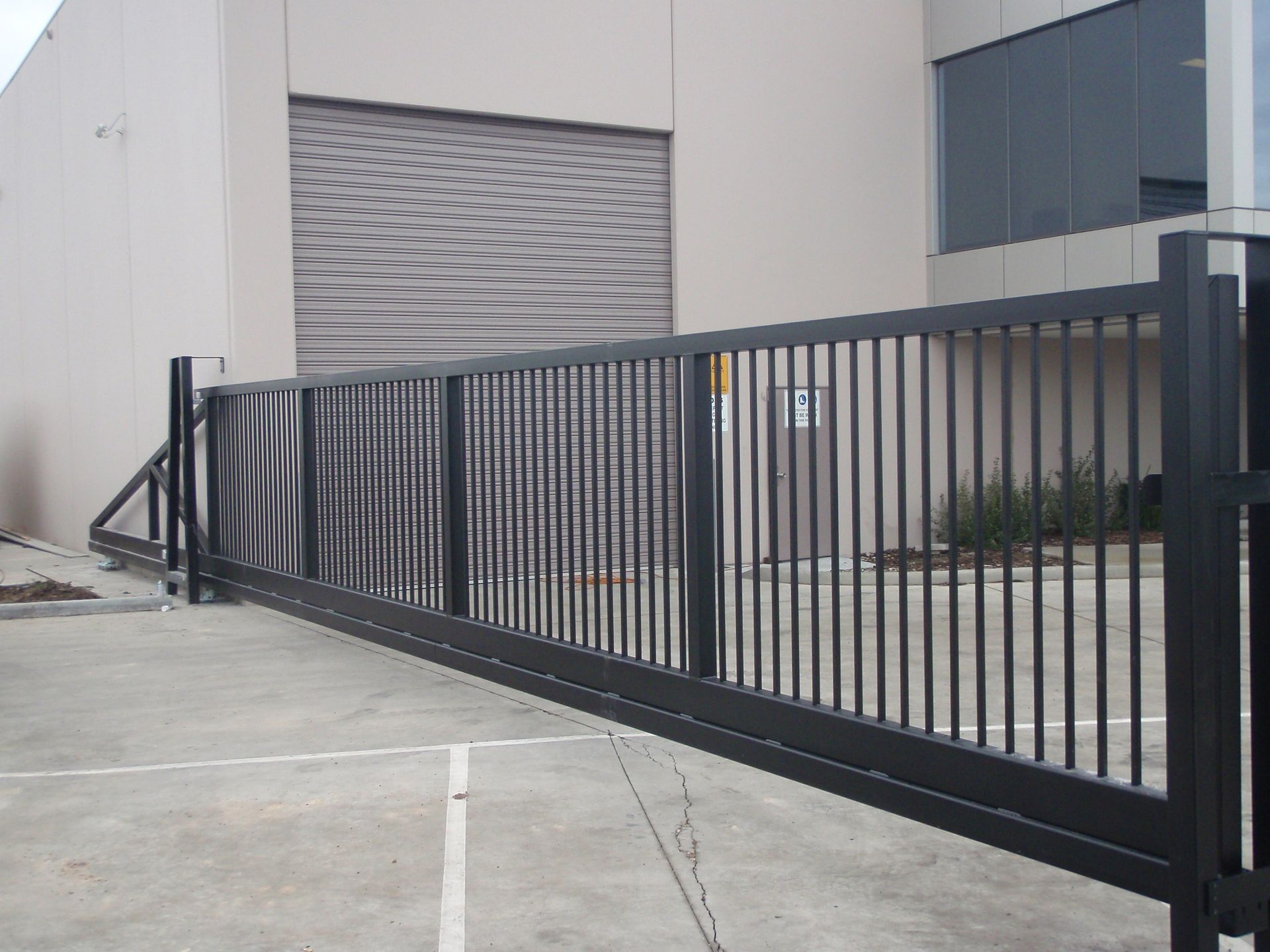 A wooden gate is open to a driveway next to a brick wall