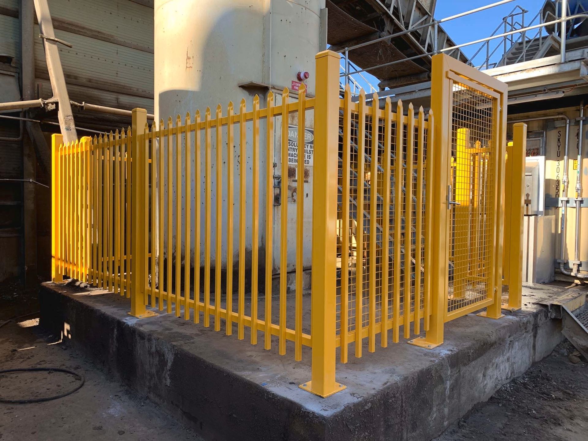 A yellow fence is surrounding a building in a factory.