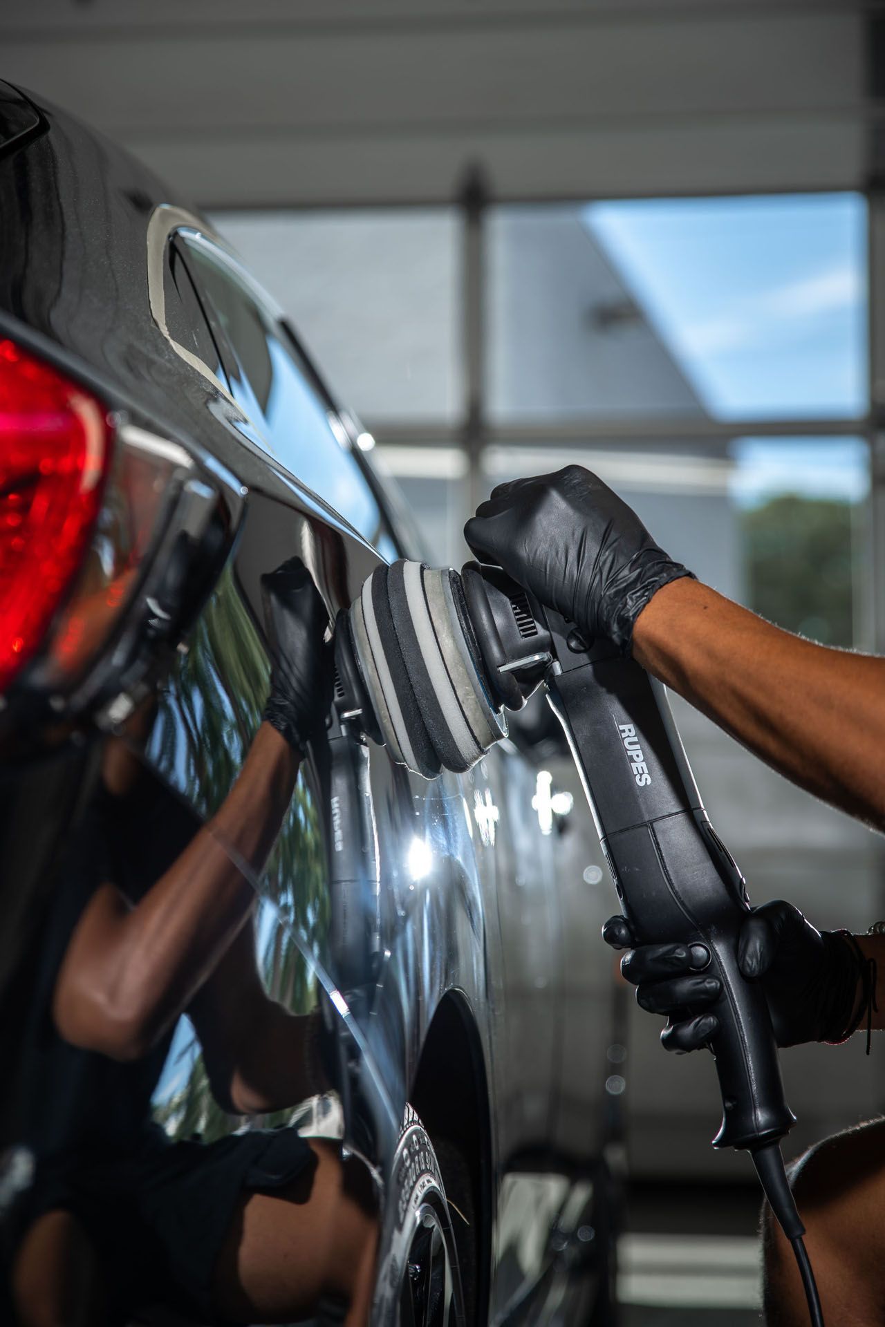 A person is polishing a car with a machine in a garage.