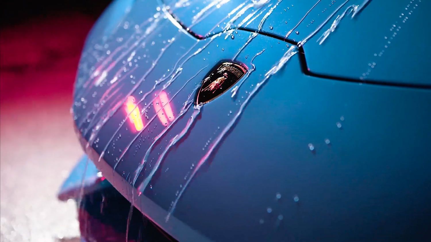 A close-up of a blue car being washed with water.