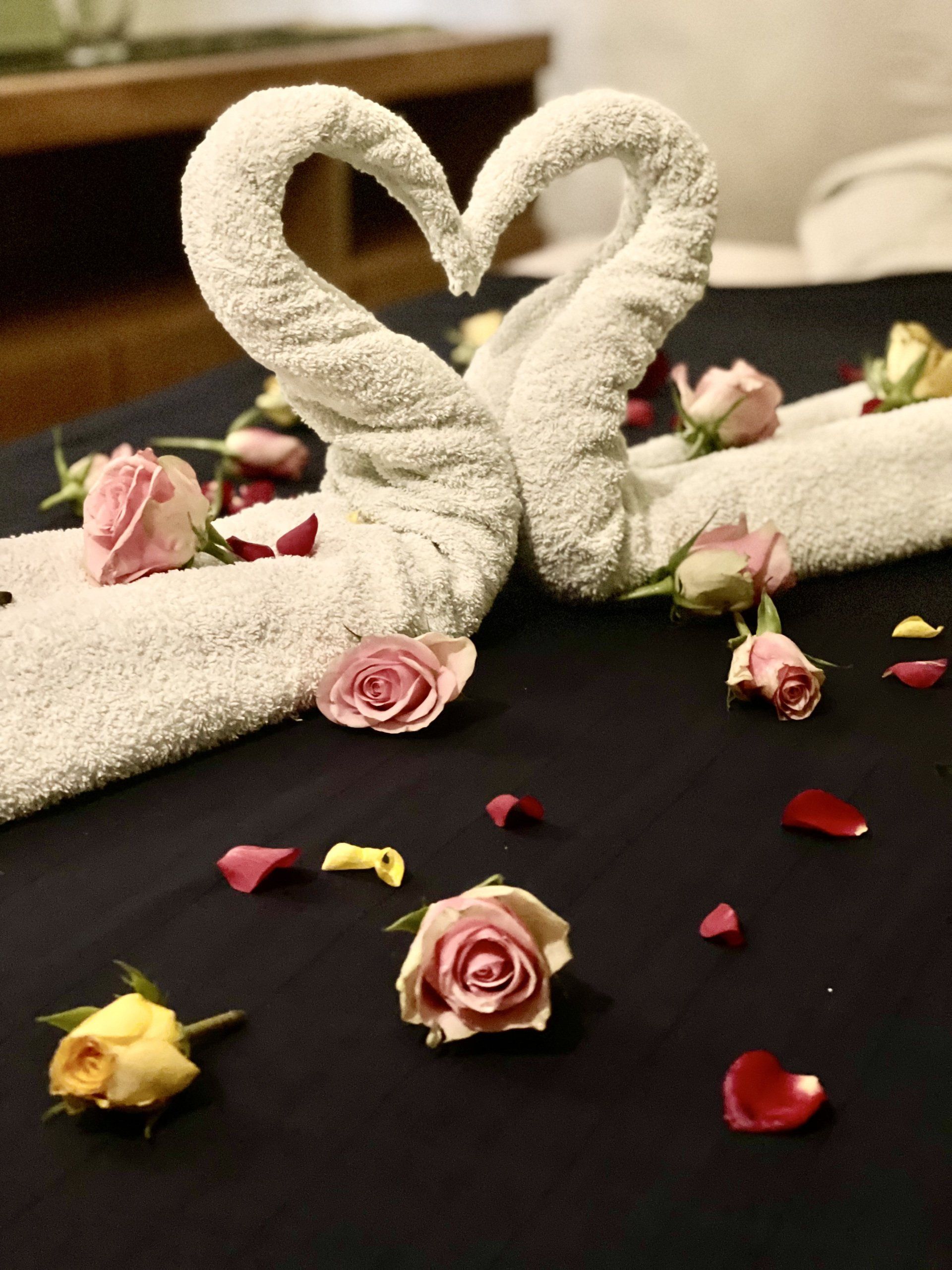 Zwei Handtücher in Schwanenform auf einem Bett mit Rosen