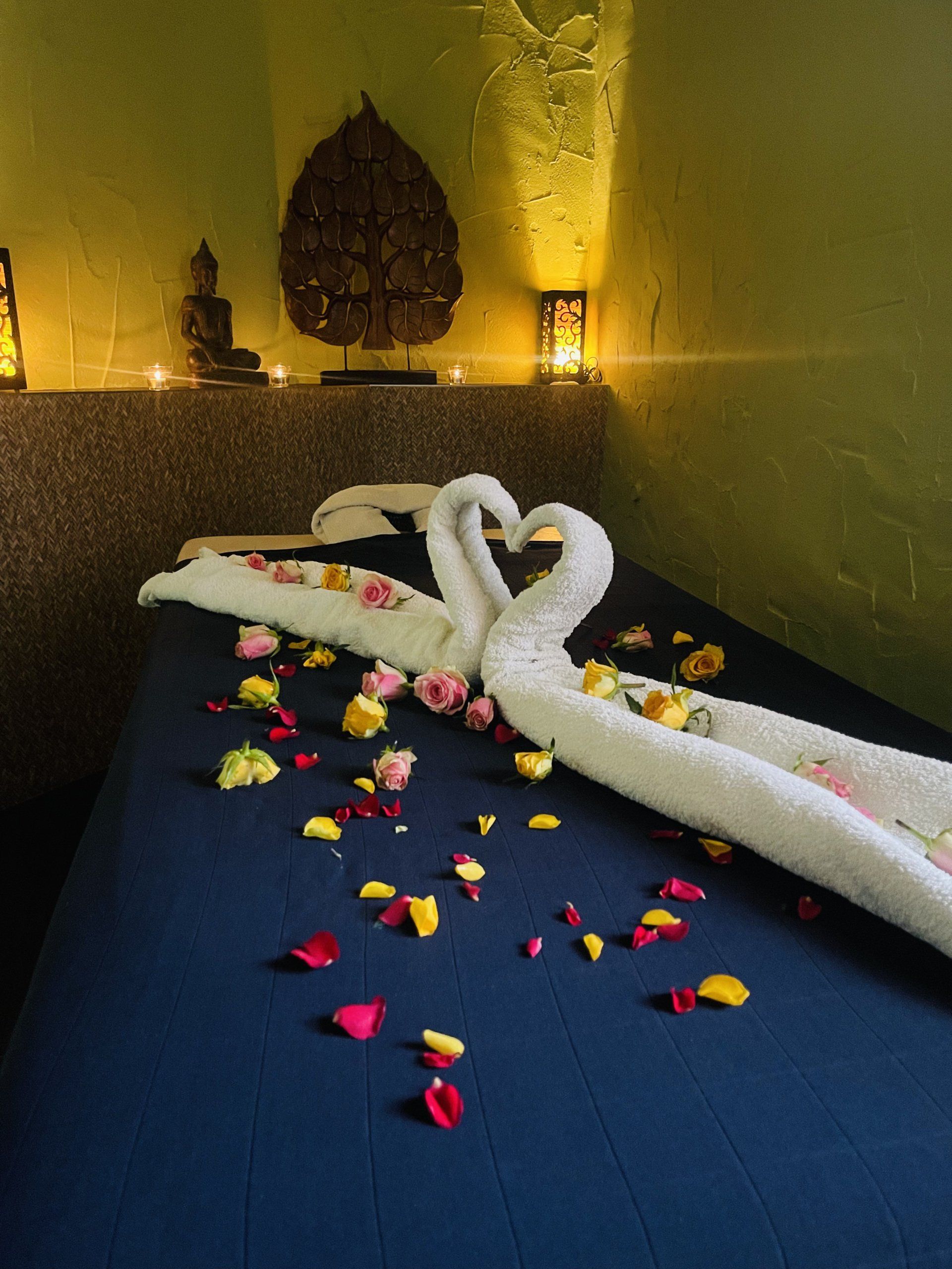 Zwei Schwäne aus Handtüchern sitzen auf einem Bett, umgeben von Blütenblättern.