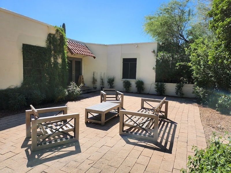 Patio with outdoor furniture on brick pavers surrounded by walls and plants under a blue sky.