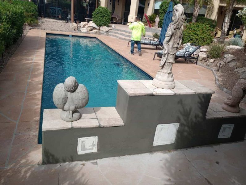 Pool with stone statues and steps, dark water. Person in yellow works in background.