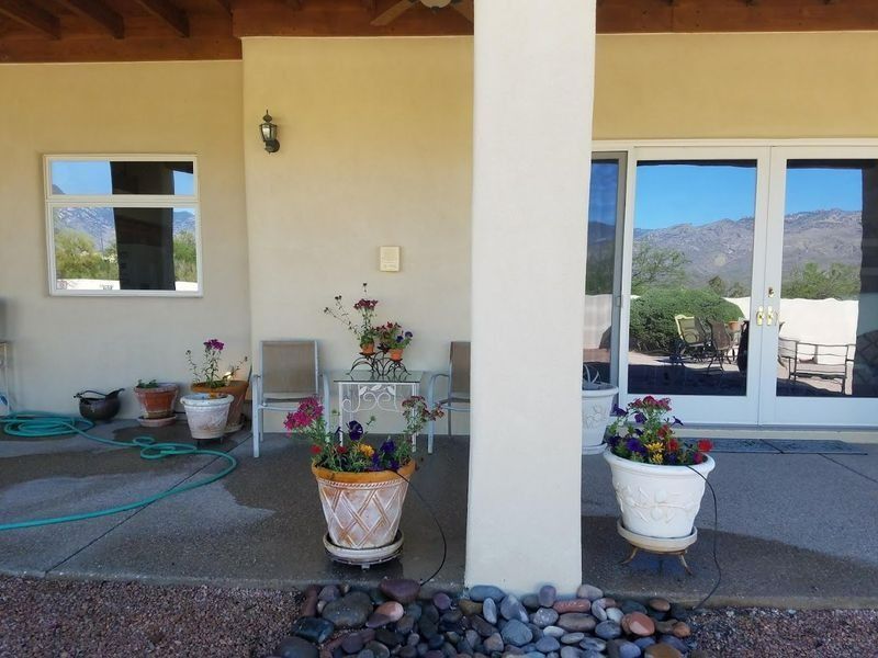 Covered patio with potted flowers, seating, and a view of mountains through a glass door.