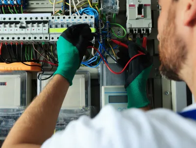 OE Services LLC - A man wearing green gloves is working on an electrical box.