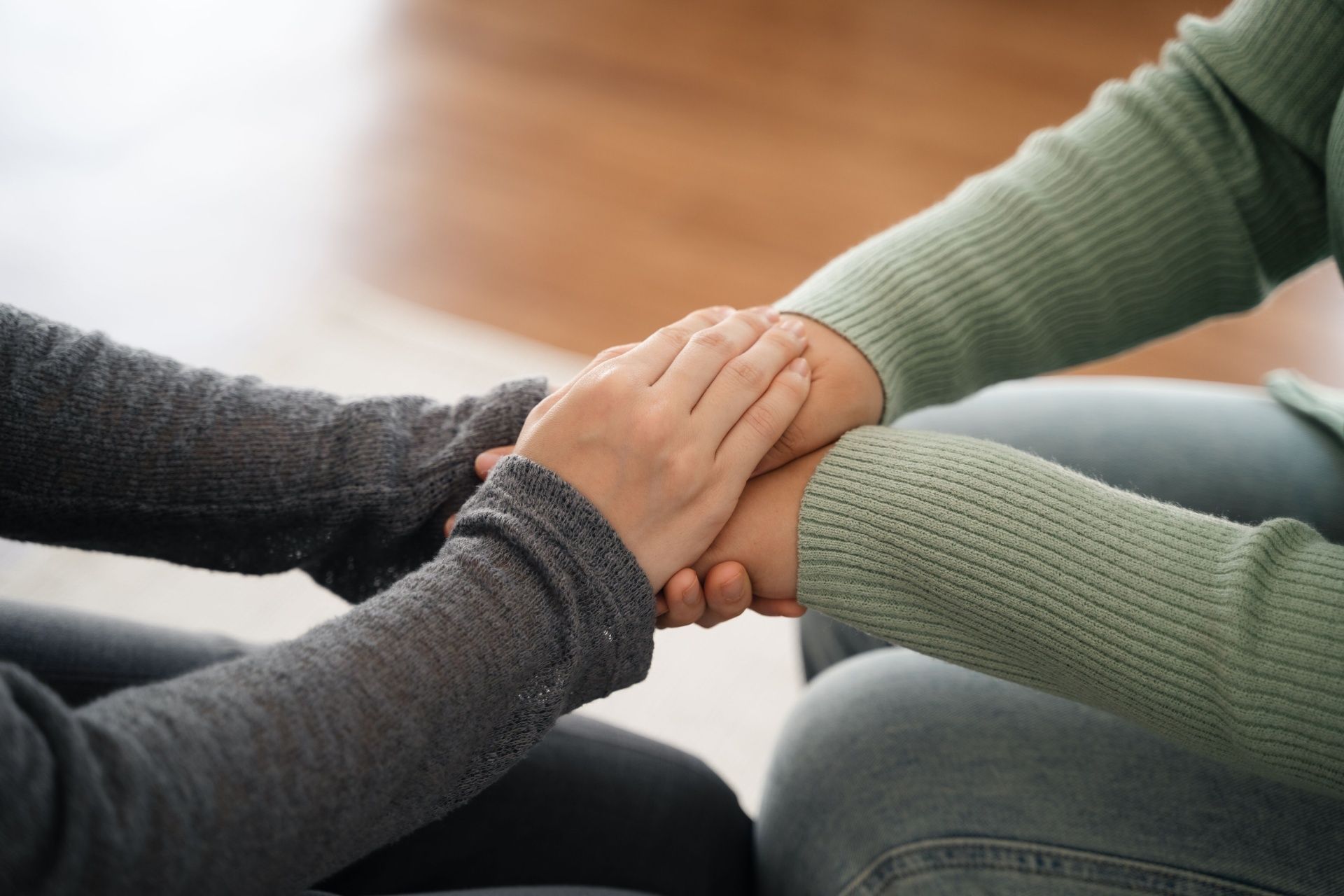 Two people hold hands in a gesture of support and comfort, with focus on their clasped hands.