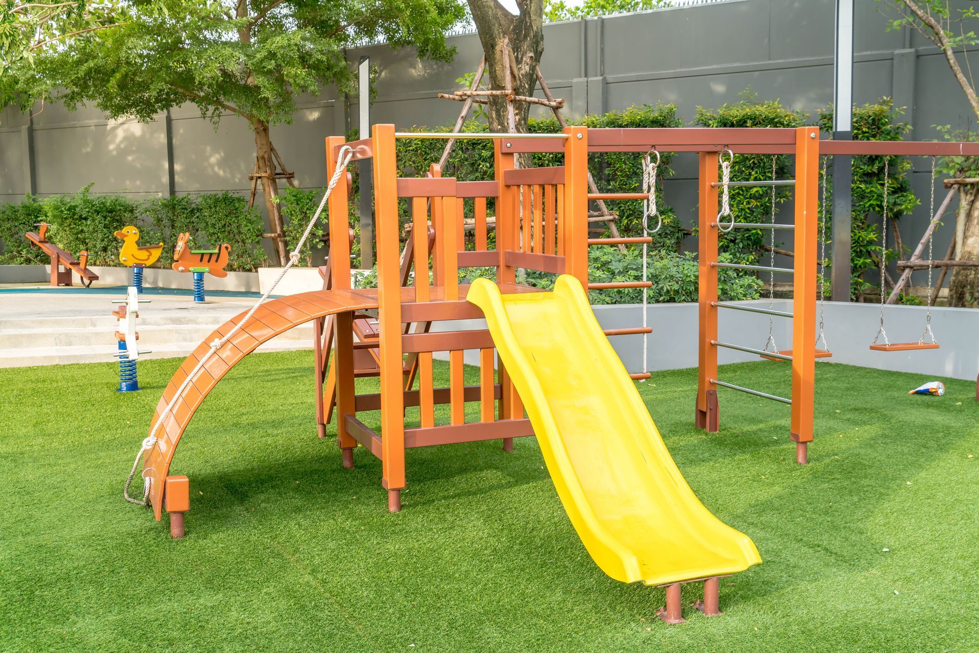 Wooden playground with a yellow slide, swings, and a rope ladder on green grass.