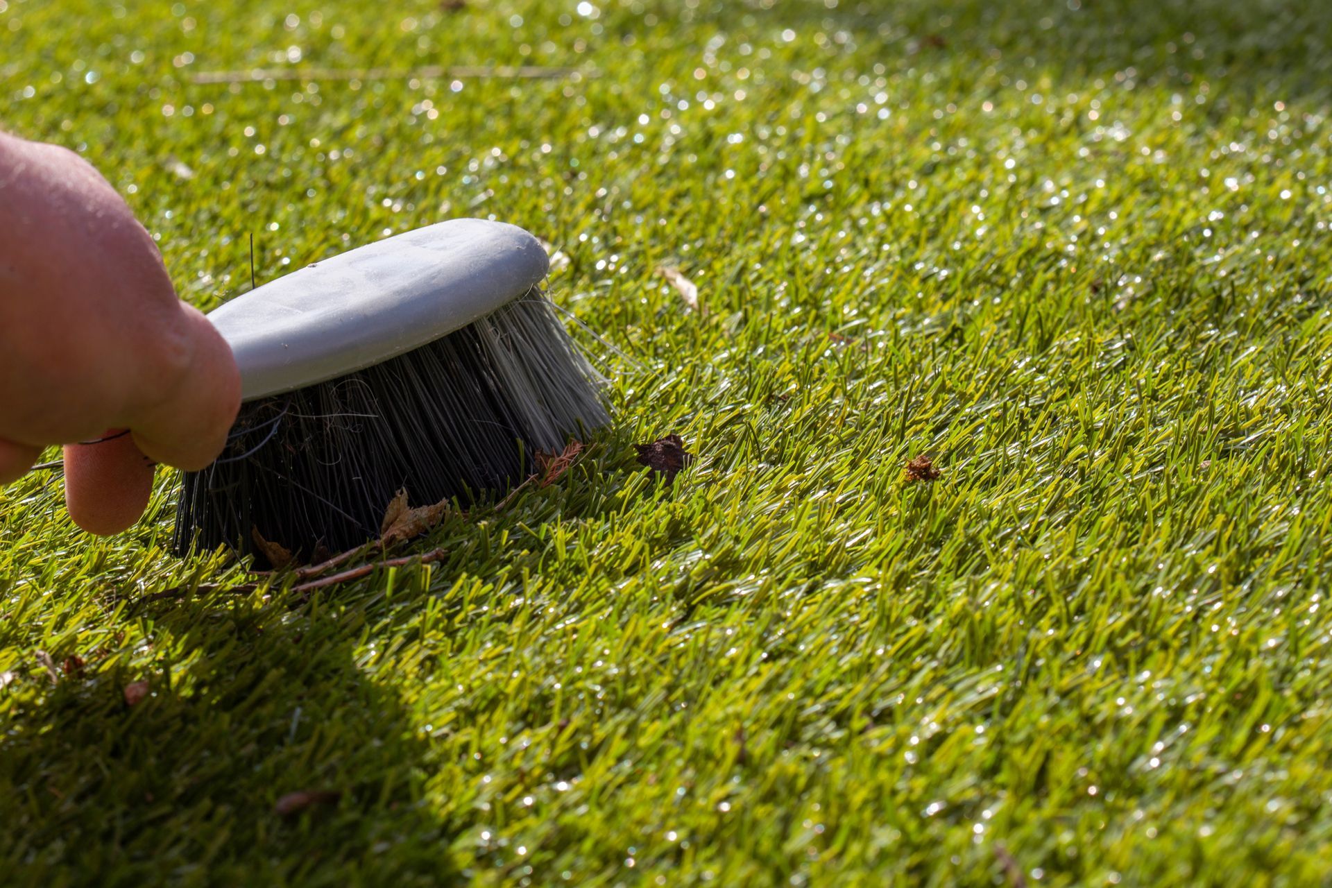 Person brushing artificial green turf with a gray brush.