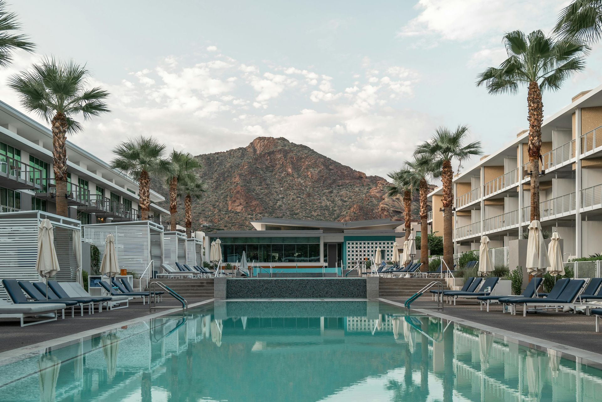 Pool at a resort with lounge chairs, palm trees, and a mountain backdrop.