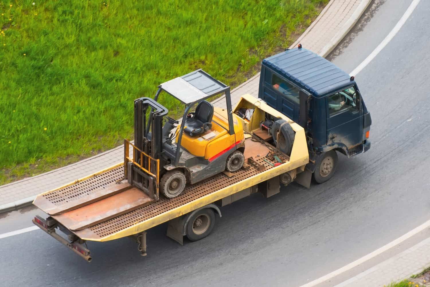A Tow Truck is Carrying a Forklift on the Back of It — Precise Plumbing & Excavations Pty Ltd in Bowen, QLD