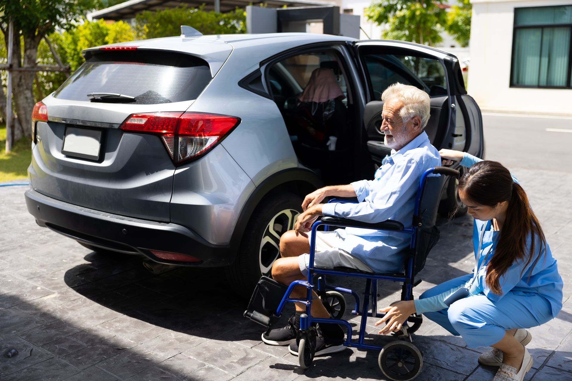 A woman is helping an elderly man in a wheelchair into a car.