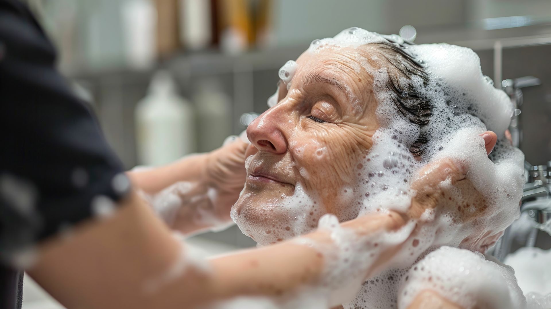 An elderly woman is getting her hair washed in a bathroom.