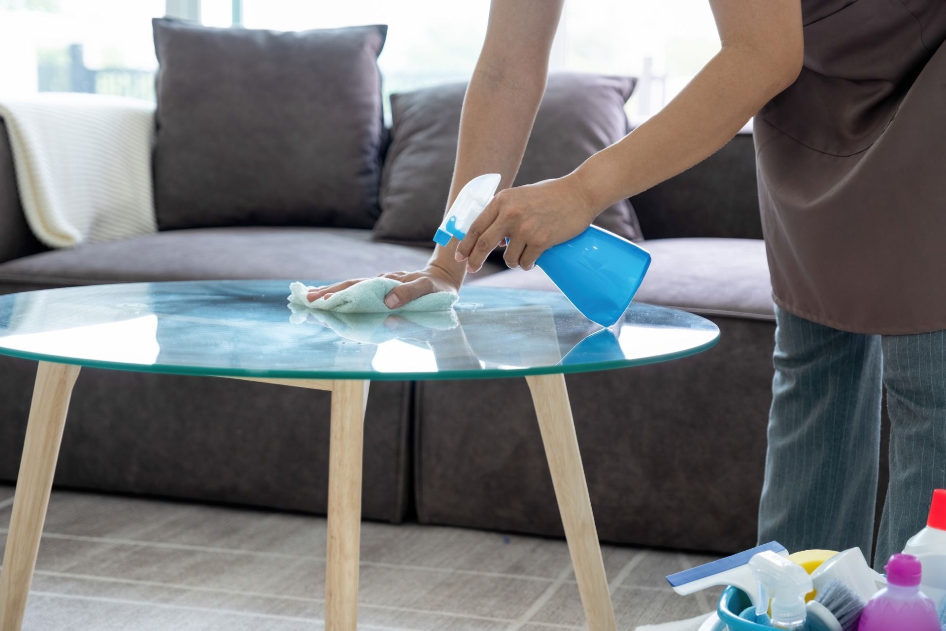 A woman is cleaning a glass table in a living room.