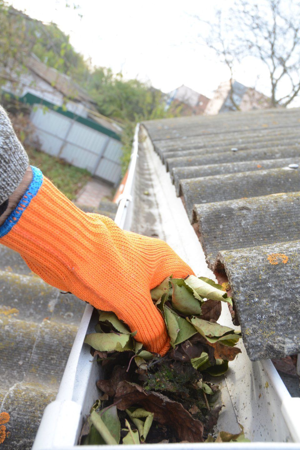 A person wearing orange gloves is cleaning a gutter with leaves.
