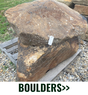 Large brown boulder with a price tag, sitting on gravel outdoors; “BOULDERS” label at bottom.